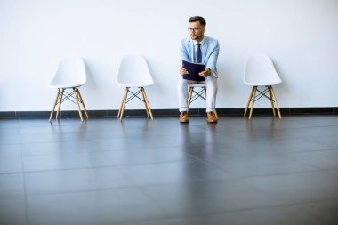 Genç adam görüşme öncesi elinde dosyayla bekleme odasında oturuyor.