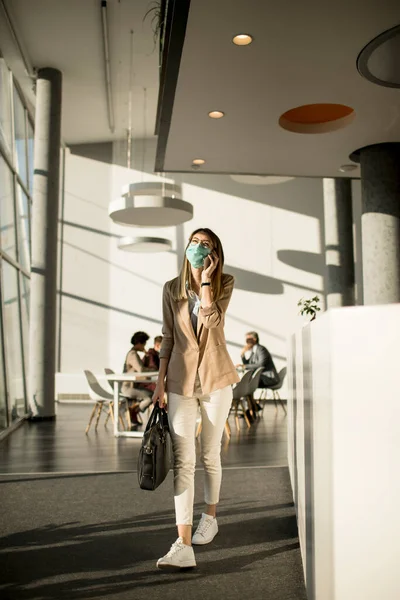 Young businesswoman on cell phone walking in the office and wearing mask as a virus protection