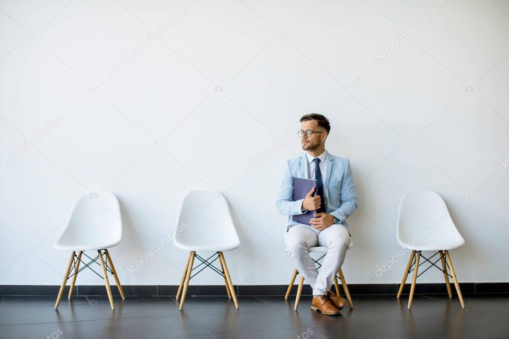 Young man sitting at chair in the waiting room with a folder in hand before an interview