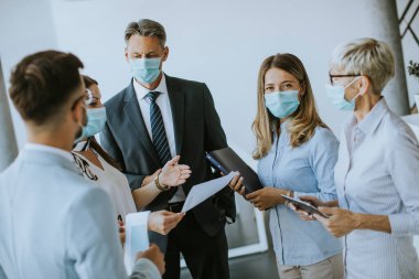 İş ortakları ofiste maske takarken ve virüs koruması takarken iş sonuçlarını inceliyor.