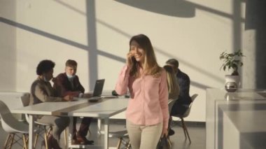 Ofiste cep telefonuyla yürüyen genç bir iş kadını.