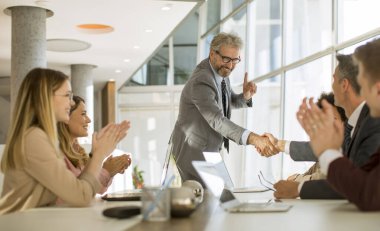 Ofisteki masada otururken iş adamları el sıkışıyor.