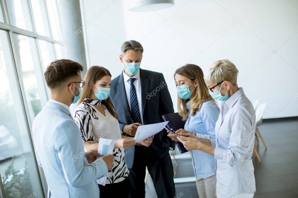 Business partners standing and looking at business results in the office while wearing face masks sa an virus protection