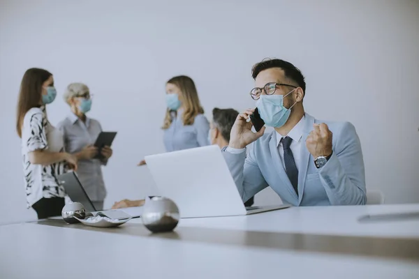 Young business man with medical protective mask works on a laptop and using mobile phone in the office