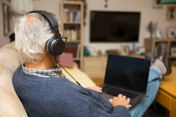 Modern elderly man siting at home with earphones and having online video call