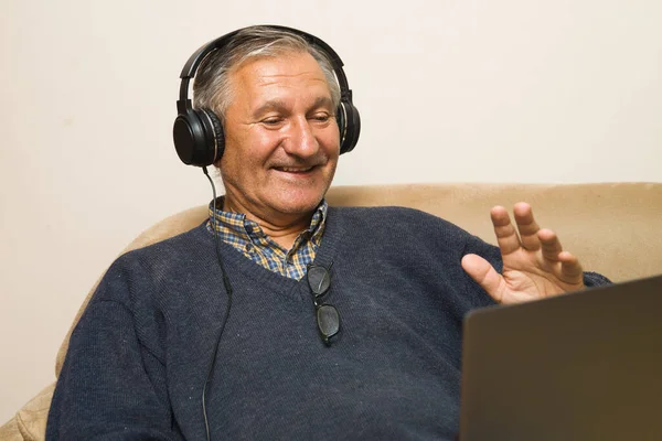 Modern elderly man siting at home with earphones and having online video call