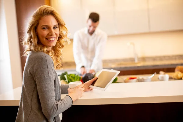 Jovem Mulher Usando Tablet Mesa Cozinha Enquanto Homem Prepara Comida — Fotografia de Stock