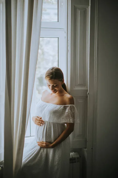 美丽的年轻孕妇在黎明时分站在房间的窗前 — 图库照片