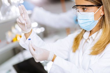 Laboratuvarda koruyucu yüz maskesi ve güvenlik Google 'ı takan kadın doktor şırınga ve ilaç şırıngası şişesini tutuyor.