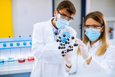 Güvenlik gözlüklü genç kimyagerler moleküler modeli laboratuvarda tutuyor.