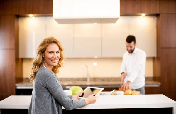 Jovem Mulher Usando Tablet Mesa Cozinha Enquanto Homem Prepara Comida — Fotografia de Stock