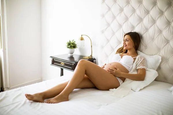 かなり若い妊娠中の女性が部屋のベッドの上に横たわっています — ストック写真