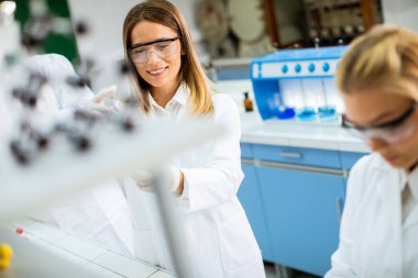 Laboratuvarda duran ve şişeyi sıvıyla analiz eden koruyucu iş elbisesi araştırmacısı hoş bir bayan araştırmacı.