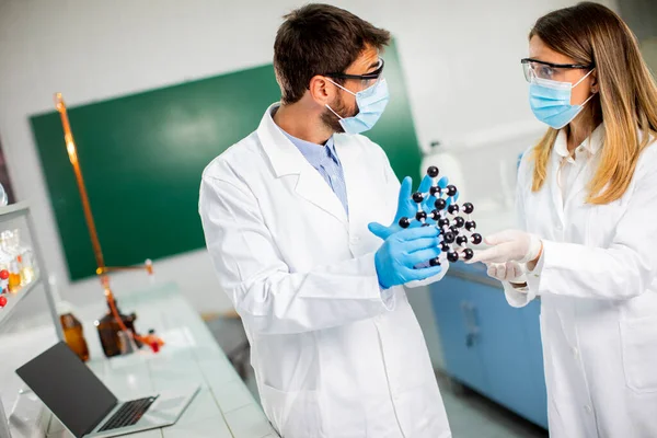 安全ゴーグルを持つ若い化学者は 研究室で分子モデルを保持しています — ストック写真