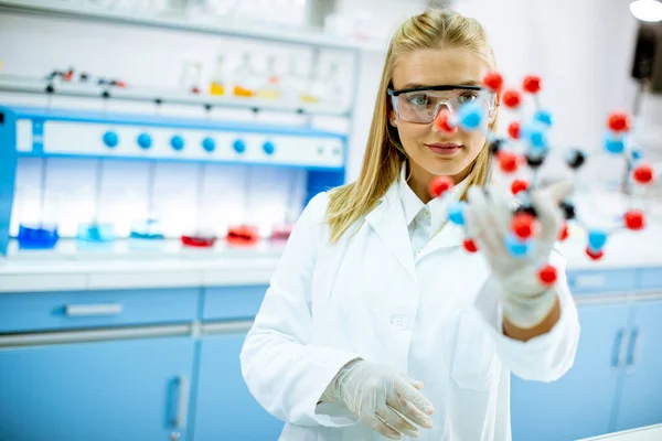 Female chemist with safety goggles hold molecular model in the lab