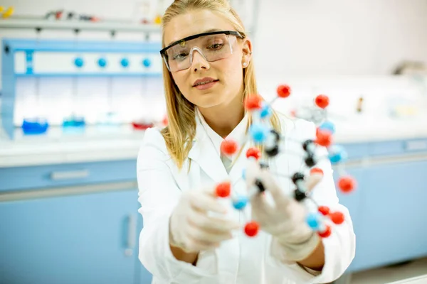 安全ゴーグルを持つ女性化学者は研究室で分子モデルを保持しています — ストック写真