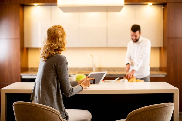 Jovem Mulher Usando Tablet Mesa Cozinha Enquanto Homem Prepara Comida — Fotografia de Stock