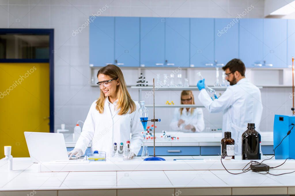 Cute female researcher in white lab coat and protective mask using laptop while working in the laboratory