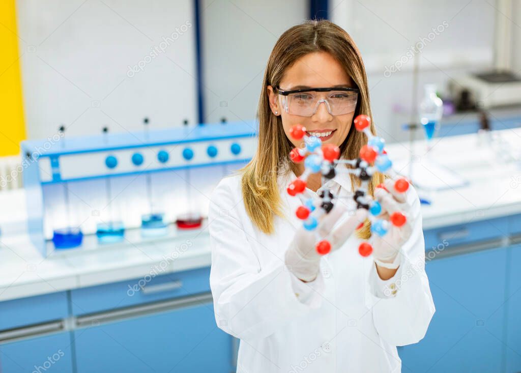 Female chemist with safety goggles hold molecular model in the lab