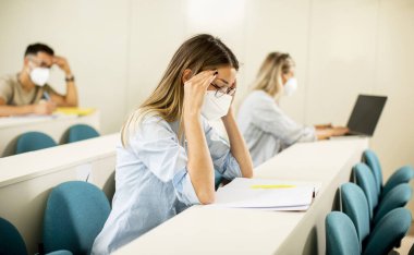 Konferans salonunda virüs koruması için yüz koruyucu maske takan genç bir kız öğrenci.