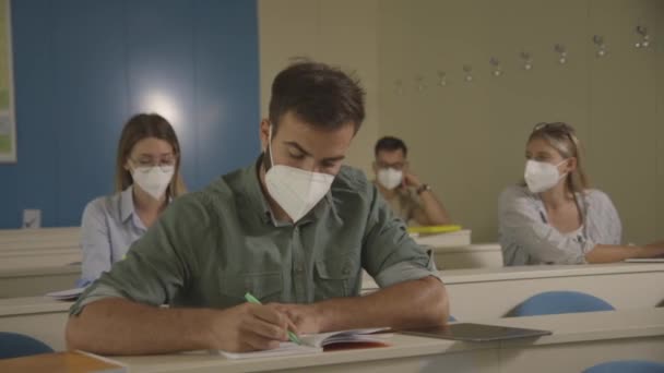 Jovens estudantes sentados na sala de aula da universidade com máscaras faciais como proteção contra vírus — Vídeo de Stock