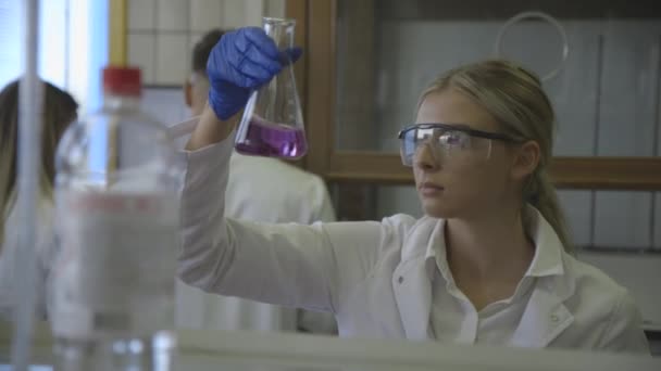 Jonge vrouwelijke wetenschapper die vloeistof analyseert in de kolf in het laboratorium — Stockvideo