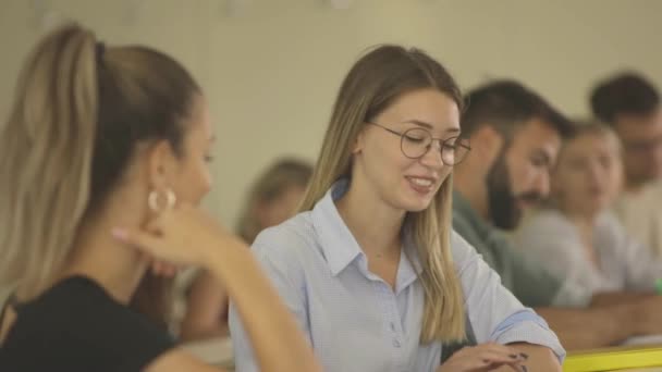 Jóvenes estudiantes sentados en el aula universitaria durante el descanso en clase — Vídeos de Stock