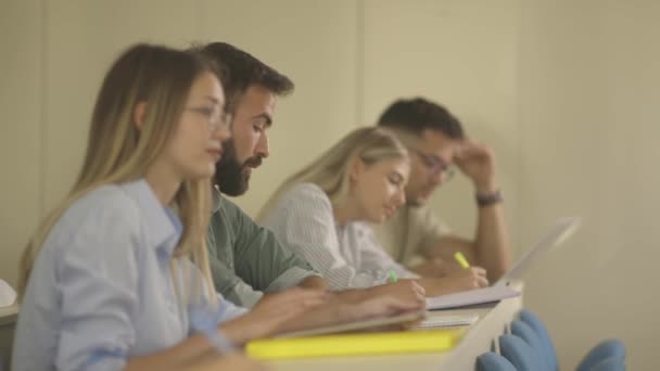 Jóvenes estudiantes sentados en el aula universitaria — Vídeos de Stock