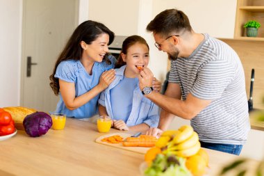 Parlak bir mutfakta, bir aile sağlıklı atıştırmalıklar hazırlarken birlikte olmaktan zevk alır. Kahkaha, meyve ve meyve suyu paylaşırken havayı doldurur, neşeli anılar yaratır..