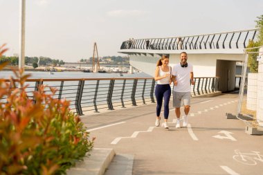 Arkadaşlar, parlak güneşli bir günde çiçek açan ve huzurlu bir deniz manzarası olan nehir kenarındaki manzaralı bir yolda koşuyorlar. Kahkahaları havayı dolduruyor..