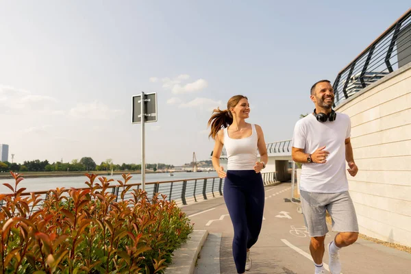 Bir çift, nehri çevreleyen canlı yeşillikler ve açık mavi bir gökyüzünün altındaki yumuşak akıntıyla birlikte öğleden sonraları sıhhatlerini kucaklayarak, liman boyunca mutlu bir şekilde koşar..