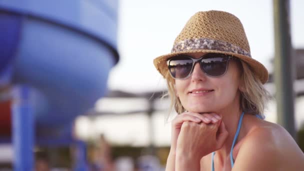 Жінка в купальнику сидить біля басейну, дивлячись на камеру посміхаючись — стокове відео