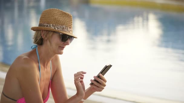 Vrouw in badmode zitten bij zwembad surfen op smart phone — Stockvideo