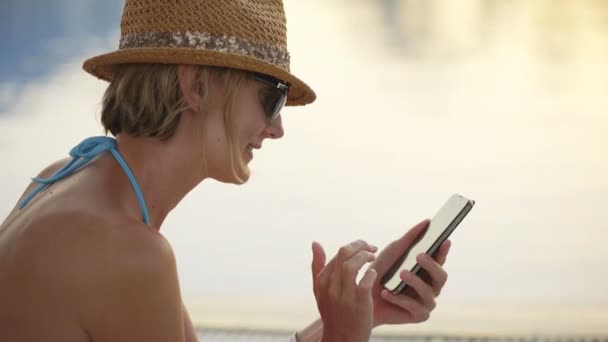 Vrouw in badmode zitten bij zwembad surfen op smart phone — Stockvideo
