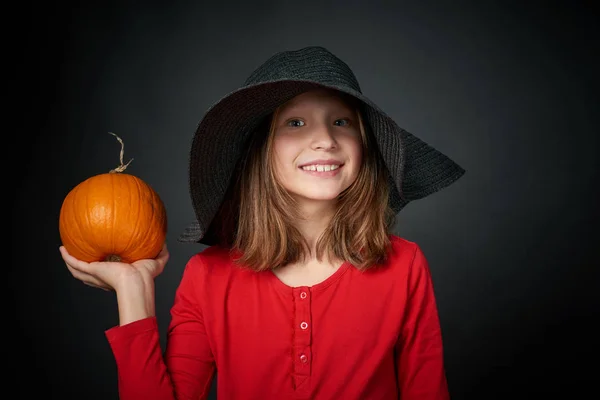 Улыбающаяся девушка в черной шляпе с оранжевой тыквой — стоковое фото