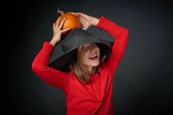 Smiling girl in a black hat holding orange pumpkin — Stock Photo, Image