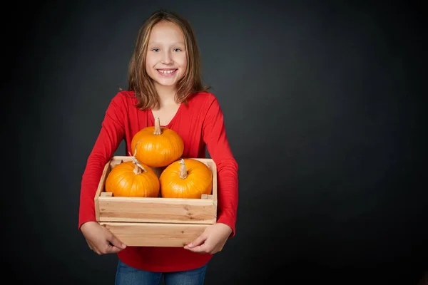 Chica sonriente sosteniendo una caja con calabazas naranjas —  Fotos de Stock