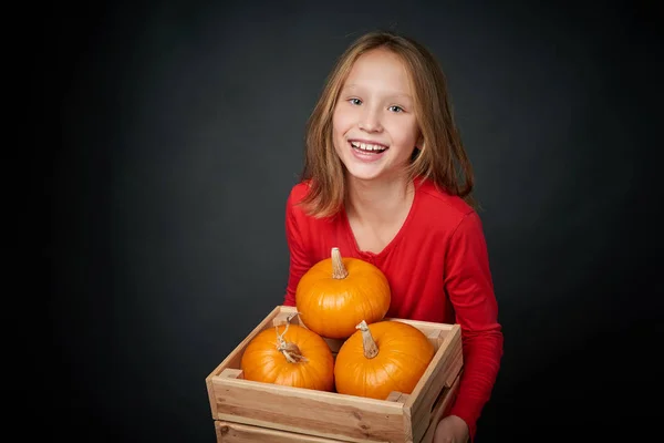 Feliz chica sonriente sosteniendo una caja de madera con calabazas maduras —  Fotos de Stock