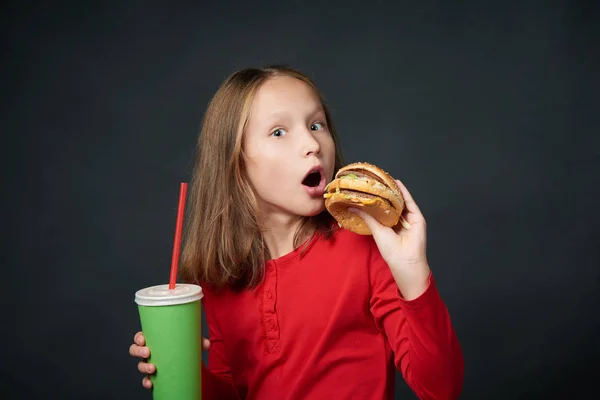 Lány fog harapni egy hamburger látszó-on fényképezőgép-meglepett pillantást — Stock Fotó