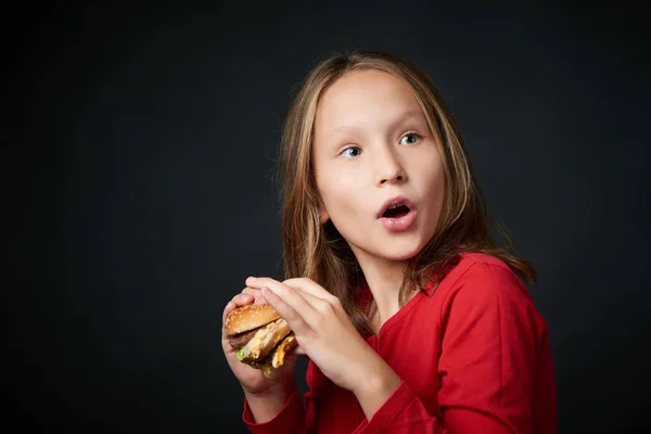 Lány fog enni egy burger visszatekintve válla fölött, tekintse meg a meglepetés — Stock Fotó