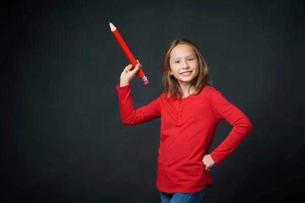 Smiling girl pointing big pencil at blank copy space for text — Stock Photo, Image