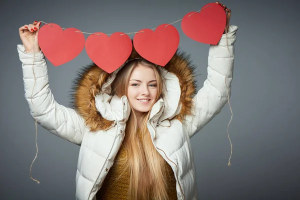 Girl in winter coat with hood on holding four hearts garland — Stock Photo, Image