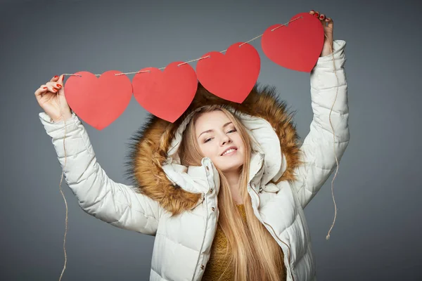 Girl in winter coat with hood on holding four hearts garland — Stock Photo, Image