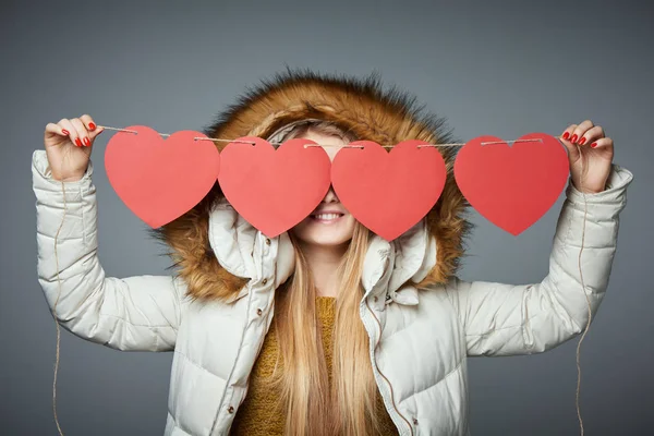 Chica en abrigo de invierno con capucha en la celebración de cuatro corazones guirnalda —  Fotos de Stock