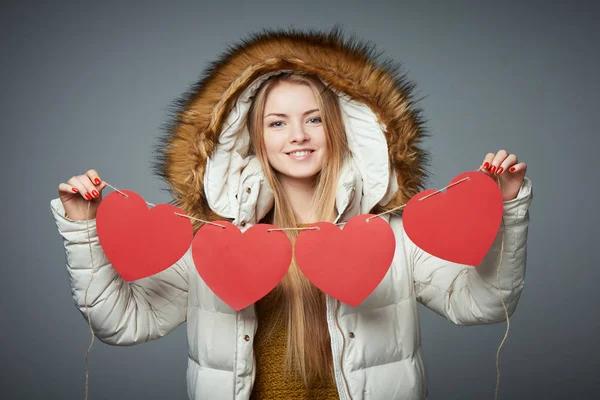 Chica en abrigo de invierno con capucha en la celebración de cuatro corazones guirnalda — Foto de Stock