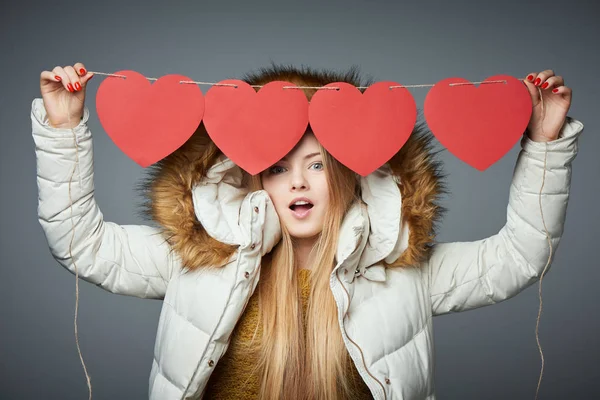 Girl in winter coat with hood on holding four hearts garland — Stock Photo, Image