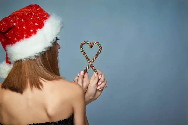 Chica en Santa Sombrero celebración de Navidad caramelos en forma de corazón —  Fotos de Stock