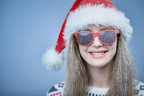 Menina congelada com neve no rosto usando chapéu de Papai Noel e óculos de sol — Fotografia de Stock
