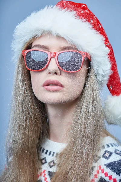 Menina congelada com neve no rosto usando chapéu de Papai Noel e óculos de sol — Fotografia de Stock