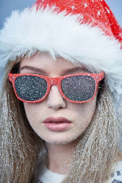 Chica congelada con nieve en la cara con sombrero de Santa y gafas de sol —  Fotos de Stock